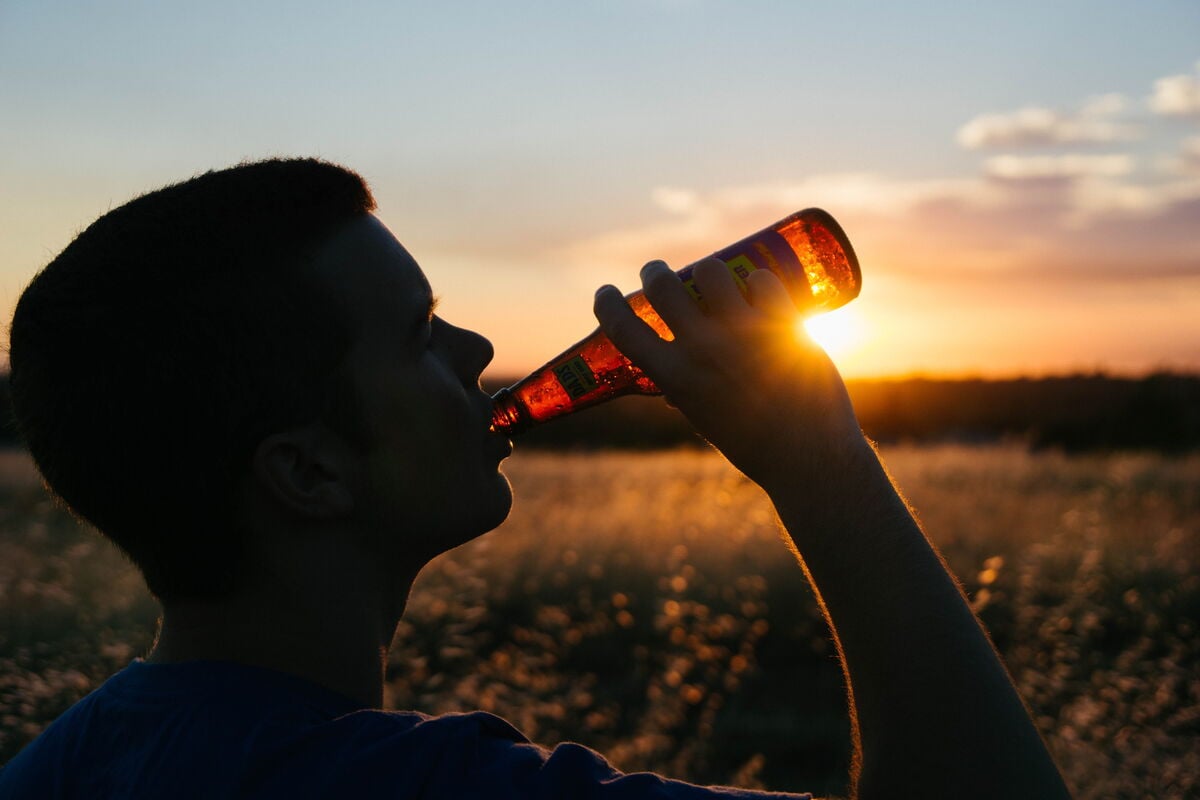 person drinking beer silhouetted by the setting sun